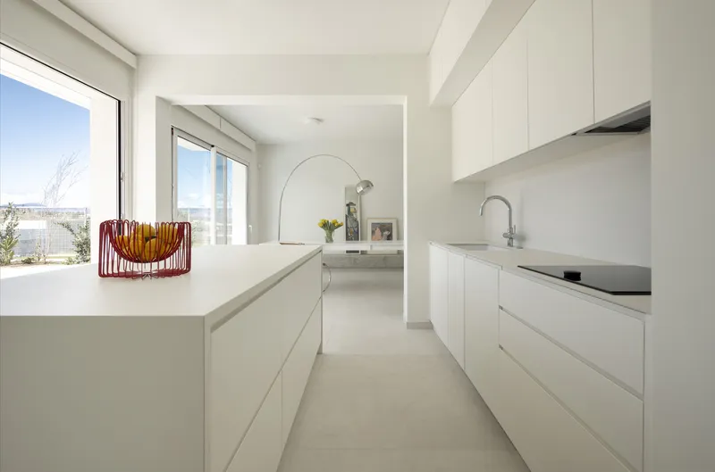 Galley kitchen with flush white cabinetry and a fruit basket near the window under clear sky