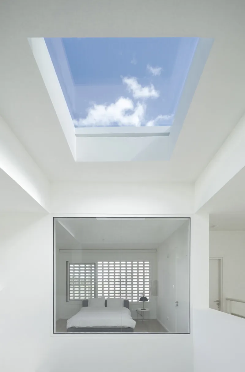 Rectangular skylight above a recessed bedroom window framing blue sky and passing clouds