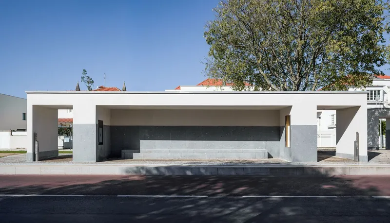 Covered shelter with concrete bench and dark wall panel framed by white columns