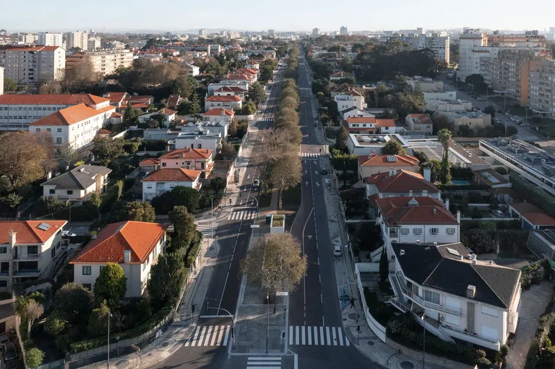 Aerial view of a linear roadway cutting through a residential neighborhood with orange rooftops