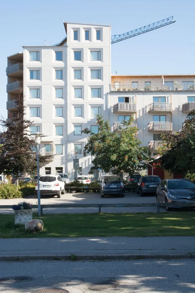 White stacked facade with punched windows viewed across a lawn with parked cars in the foreground