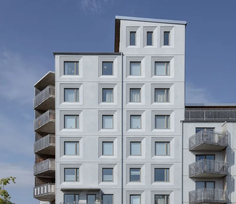 White facade with grid of framed windows flanked by balconies with vertical screening under blue sky