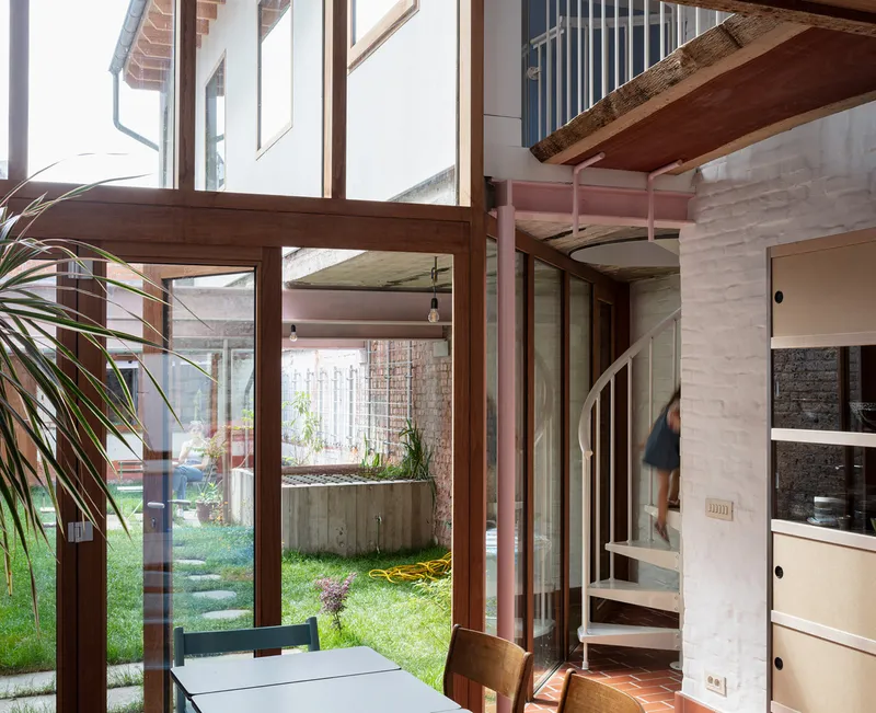 Interior view from dining area through timber-framed glazing to courtyard garden with spiral staircase and concrete planter