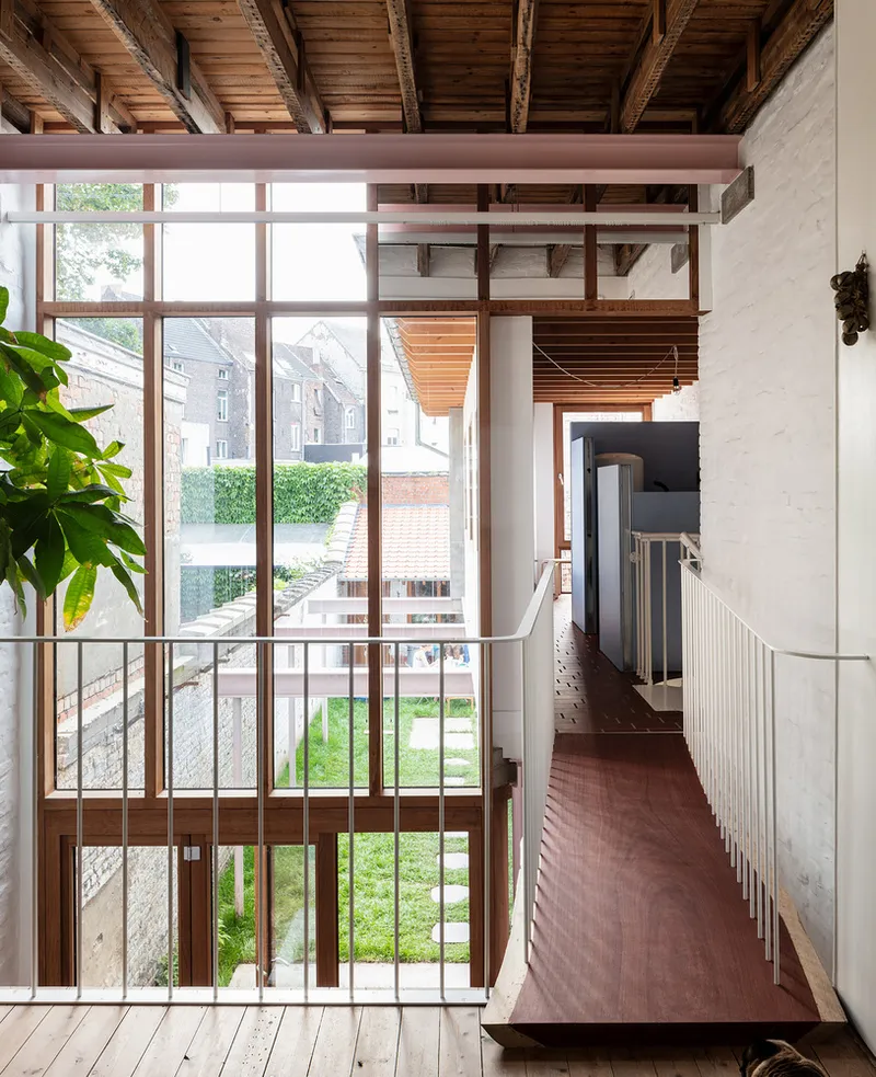 Upper level hallway with timber ceiling beams overlooking courtyard through full-height glazing and metal railing