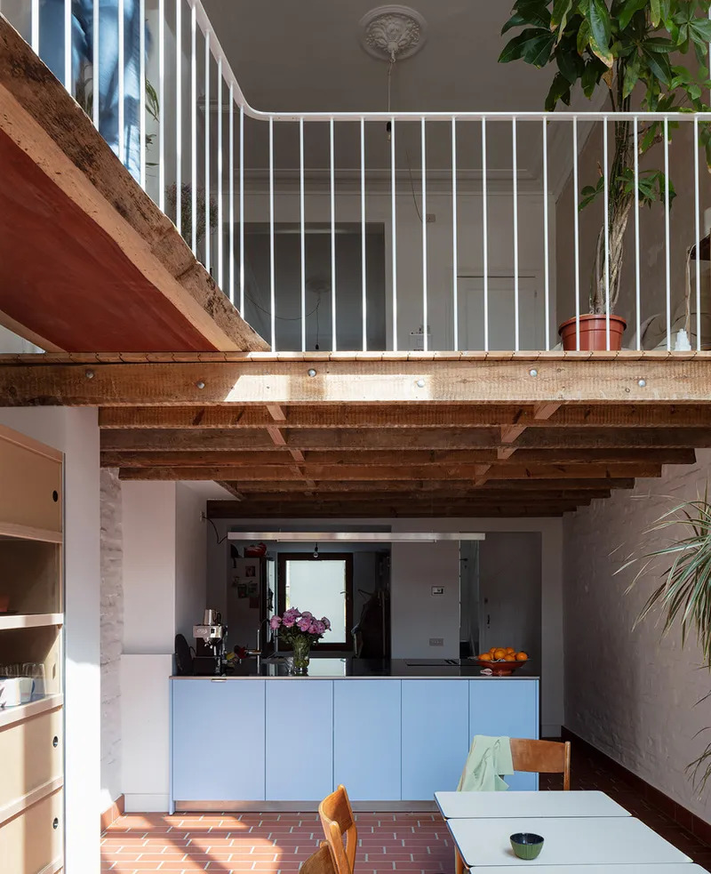 Open kitchen with exposed timber joists above mezzanine with white vertical railings and potted plants