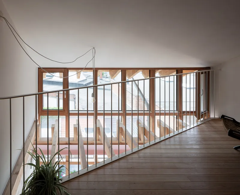 Upper level hallway with steel railing overlooking timber-framed windows and a planted courtyard below