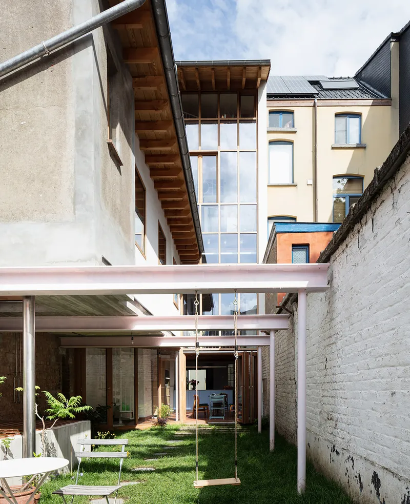 Courtyard with lawn and rope swing beneath steel beam canopy framed by painted brick party walls