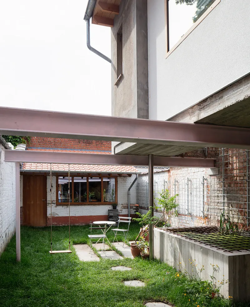 Courtyard view with pink steel beams spanning between white stucco walls and a grass lawn below