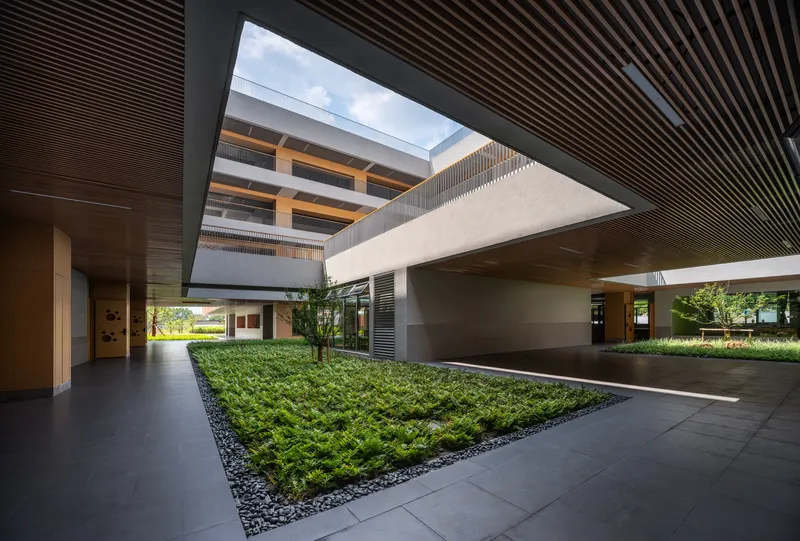 Central courtyard with planted beds and small trees beneath a rectangular skylight framed by timber-slatted ceilings