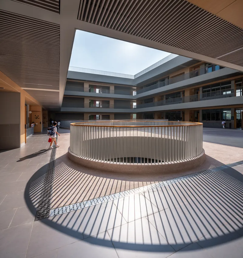 Circular timber-screened opening in the courtyard floor casting radiating shadows under midday sun