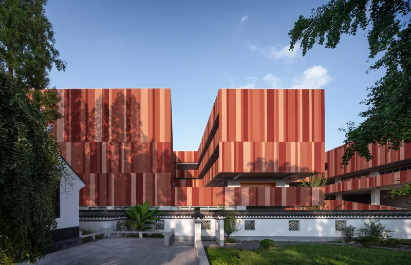 Striped terracotta panel facade rising above a white traditional perimeter wall with ornamental details