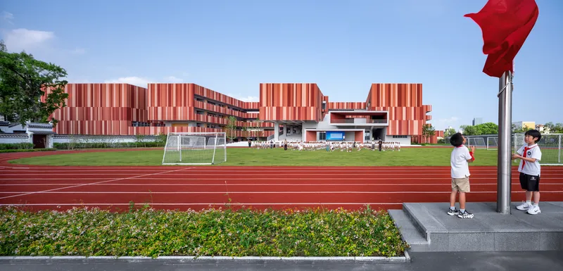 View across the running track toward the striped facade with students and red flag in foreground
