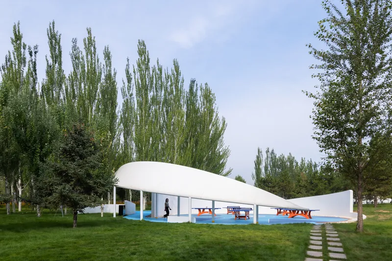 White curved canopy structure with blue platform spanning across a lawn dotted with poplars and deciduous trees