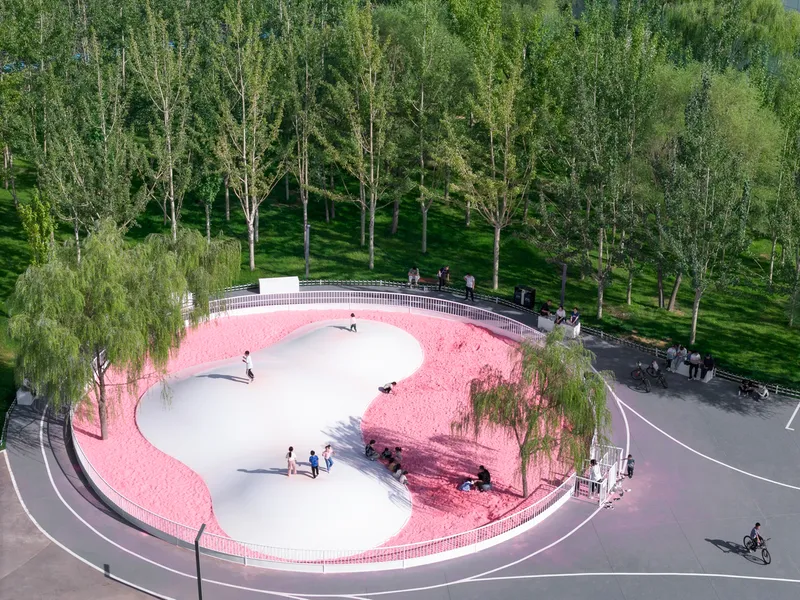 Aerial view of circular white play area surrounded by pink gravel and curved railing in a tree-lined park