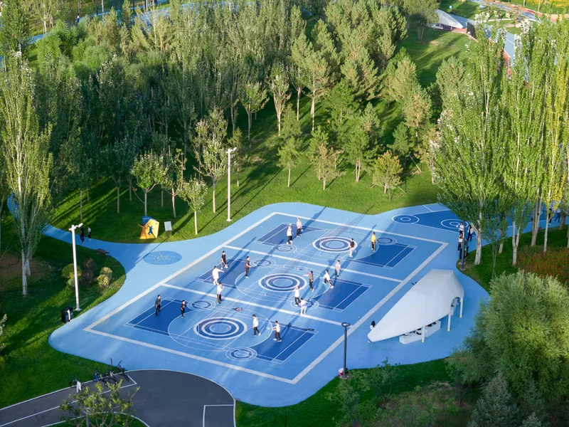 Overhead view of blue patterned play court with circular and geometric markings surrounded by green lawn and trees
