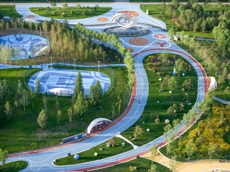 Aerial view of serpentine pathways connecting circular pavilions and sports courts through planted landscape in afternoon light