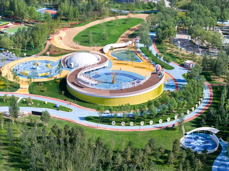 Spiral ramped water feature with yellow and brown banding encircling blue pools within a landscaped park setting
