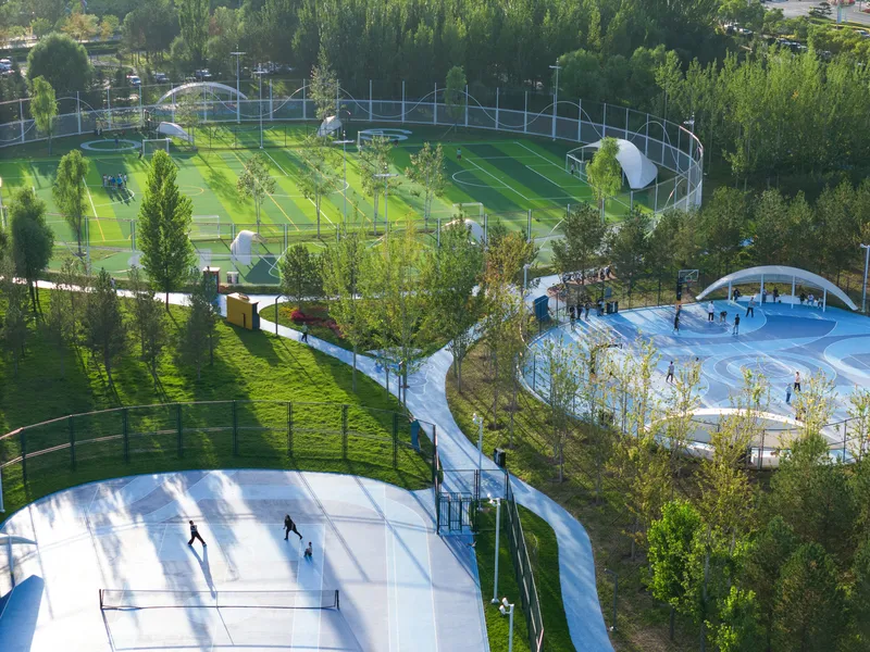 Elevated view of white sports court with tennis and basketball areas winding through green fields and tree groves