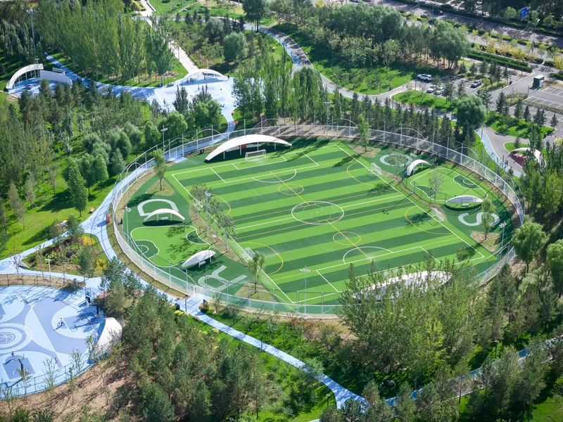 Aerial view of the oval sports pitch encircled by pedestrian paths and dense tree plantings in summer
