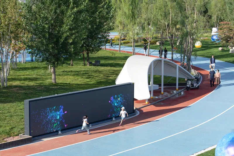 Curved white canopy shelter along a terracotta pathway with children playing and interactive digital screen wall