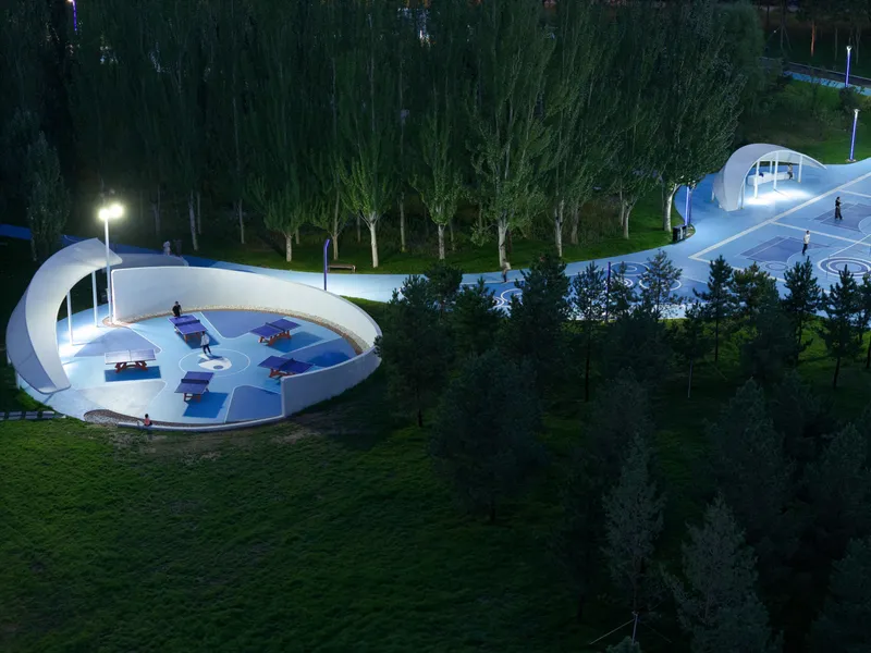 Night view of the circular basketball platform with white canopy shelter and artificial lighting among trees