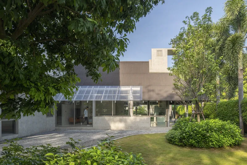 Garden view of the corrugated metal roof with translucent panels above a gravel courtyard and palms