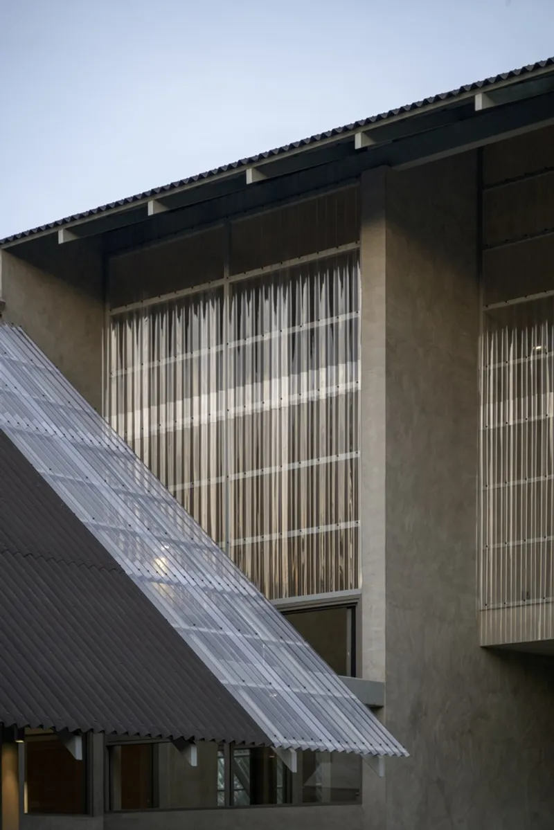 Concrete facade with vertical louvered screens and a translucent corrugated canopy at dusk