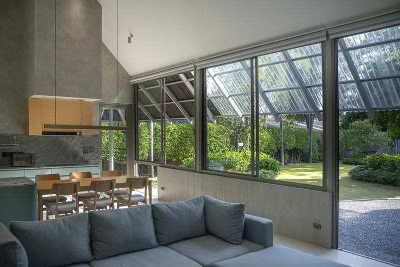 Open-plan living area with floor-to-ceiling glazing framing the garden and exposed corrugated roof structure overhead