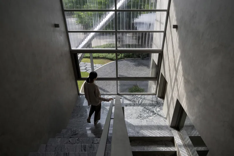 Top-down view of a person descending the staircase beside a full-height glazed wall overlooking the courtyard