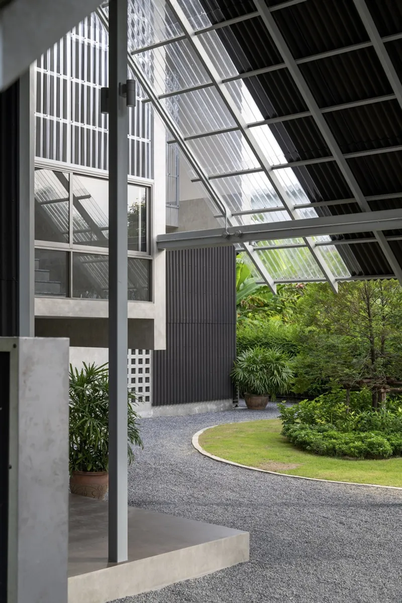 Covered entry courtyard with sloped glazed roof and gravel path winding through planted beds