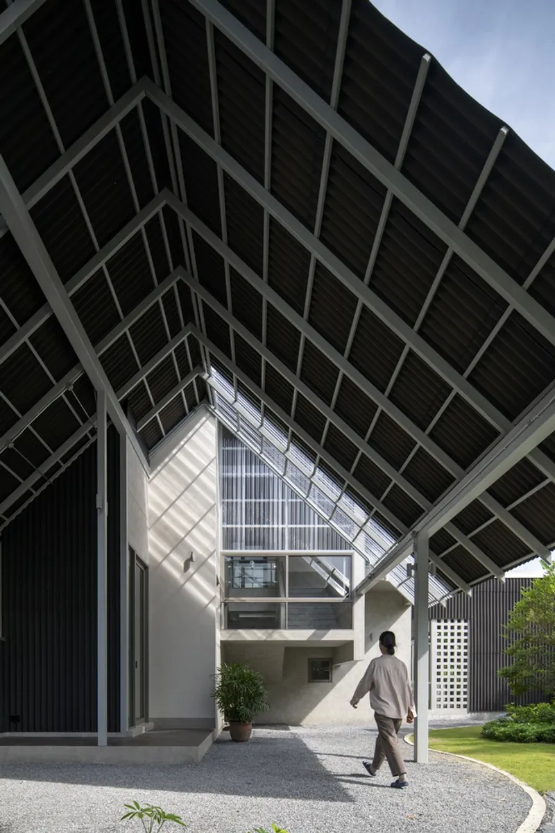 Concrete volumes with corrugated metal cladding beneath the triangular steel framework roof as a figure walks through