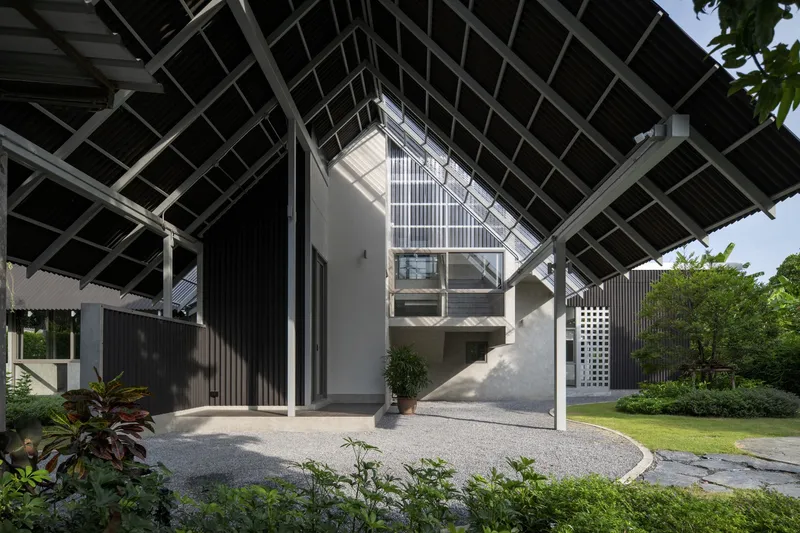 Entry plaza with gravel surface beneath the triangular pitched roof structure surrounded by potted plants