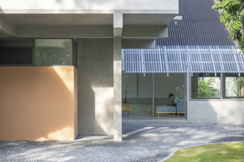 Covered concrete porch with peach-colored wall element and corrugated metal canopy in dappled sunlight