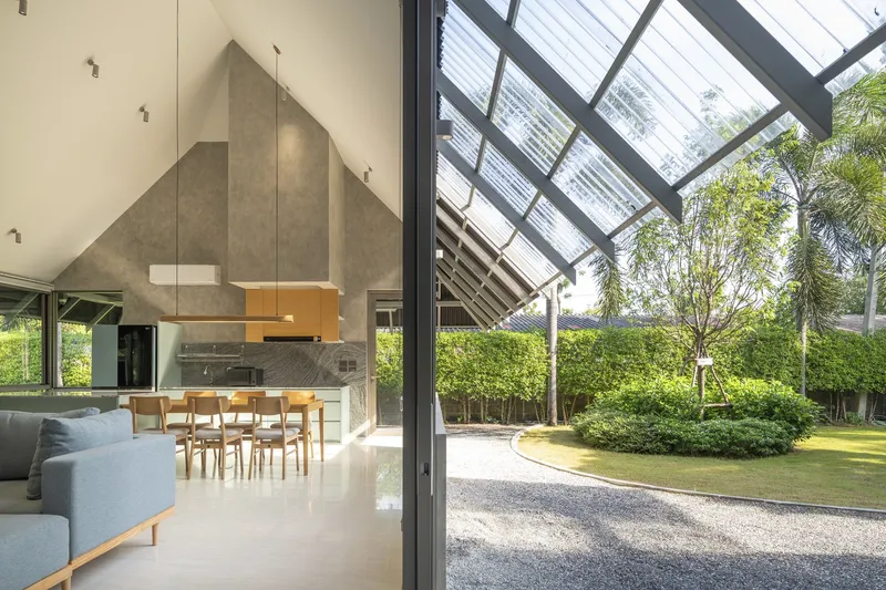 Double-height living space beneath the angled translucent roof with palm trees visible through the open threshold