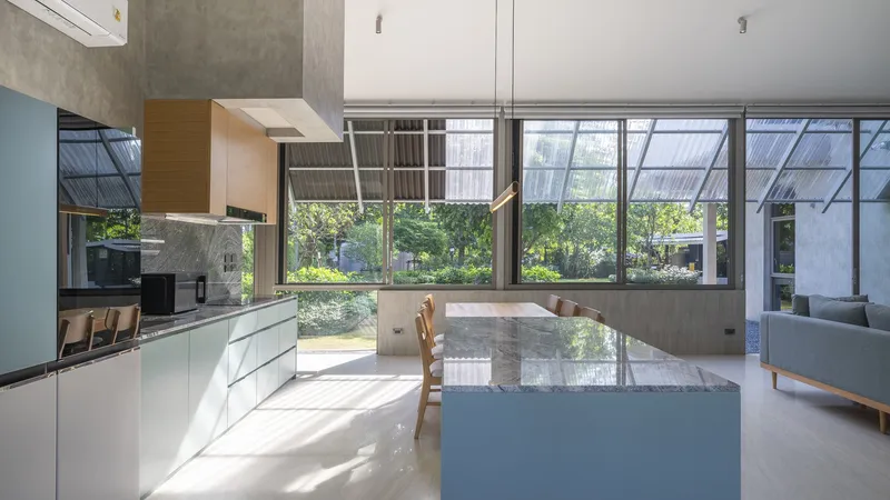 Open kitchen and dining space with marble island beneath exposed concrete beams and glazed courtyard views