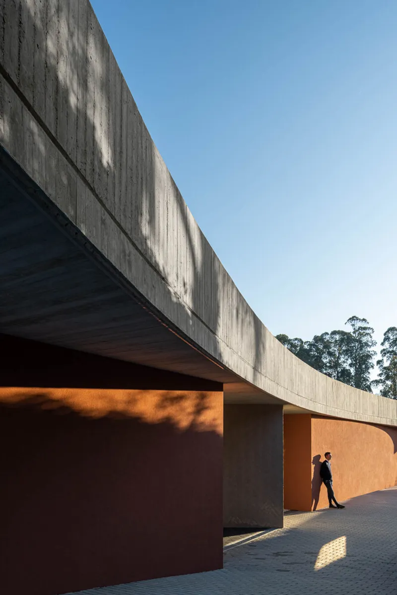 Concrete overhang with board-formed soffit above orange stucco walls and a figure in late afternoon light