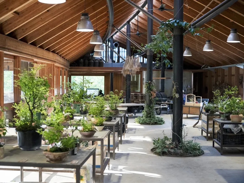 Interior greenhouse space with planted beds, industrial pendant lights and timber-clad gabled ceiling