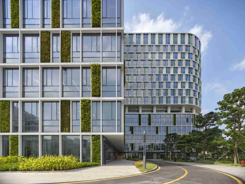 Curving driveway leading to the podium entrance framed by vertical greenery panels and a cylindrical glass facade