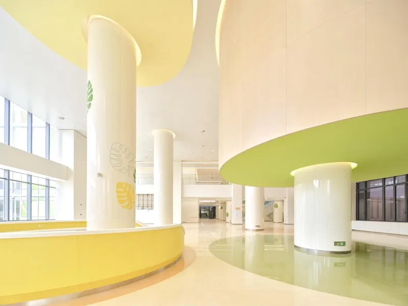 Interior atrium with white cylindrical columns, yellow curved desk, and chartreuse ceiling disc above polished floors