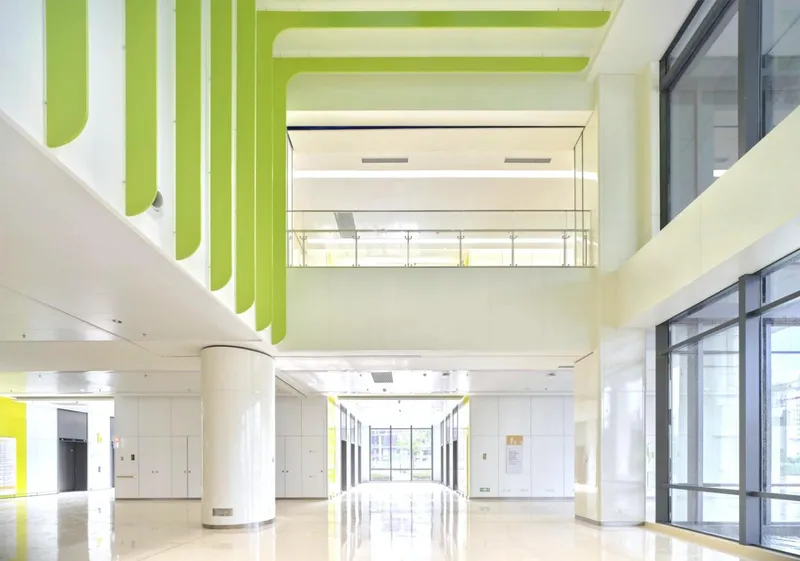 Double-height lobby with white columns, polished floor, and lime green ceiling baffles overhead