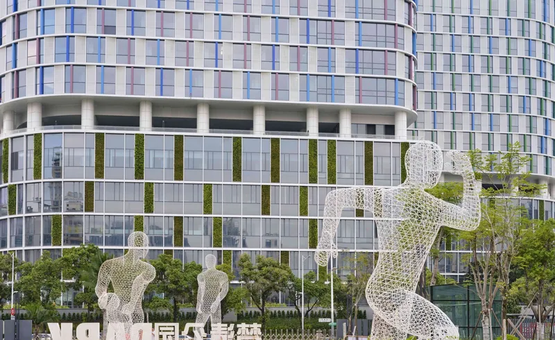 White mesh figural sculptures in foreground with glazed podium facade featuring vertical green wall panels behind