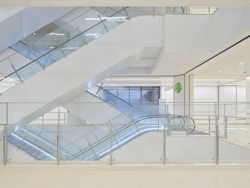 Crisscrossing escalators with glass balustrades connecting multiple levels in a daylit interior atrium