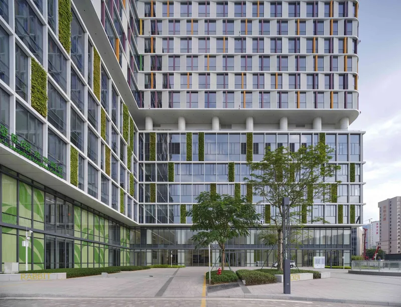 Courtyard plaza with young trees and vertical green walls integrated into the transparent glass podium