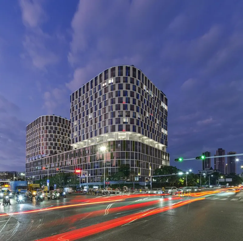 Corner view at dusk with illuminated podium and vehicle light trails streaking across the wet roadway