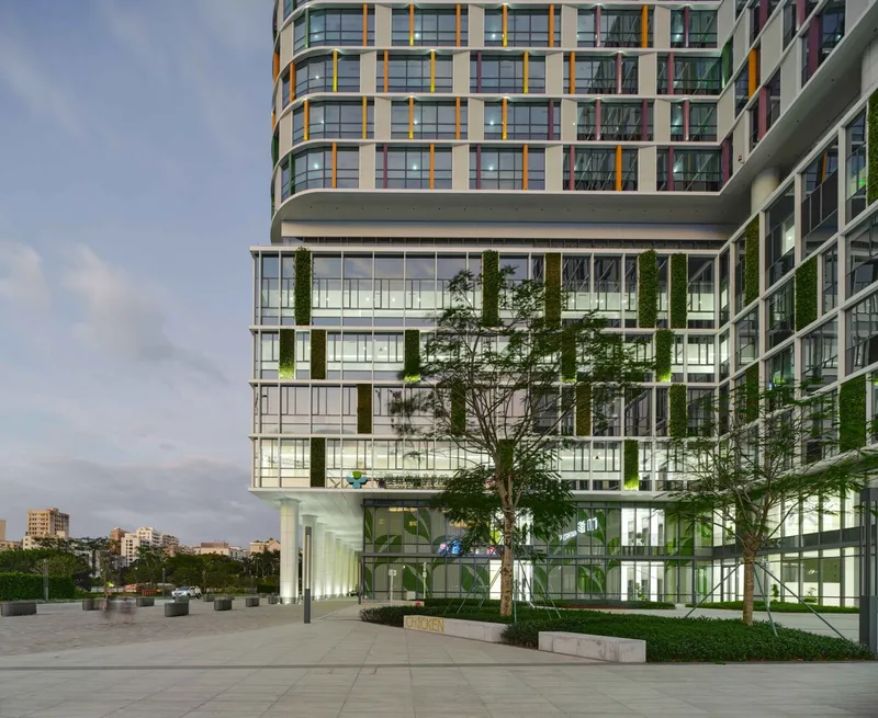 Glass podium facade at twilight with vertical planted columns and trees in planters on the plaza