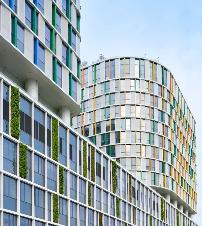 Facades with vertical green planting strips and multicolored panelwork on curved and rectilinear towers under soft daylight