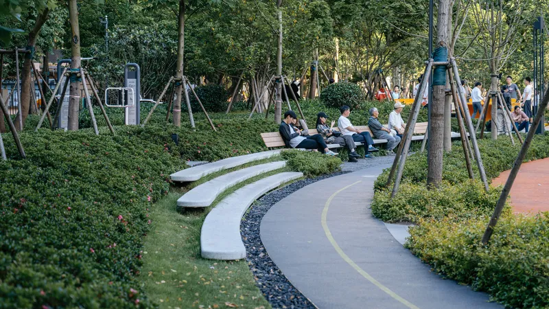 Curved concrete seating terraces beside the pathway with visitors resting among hedges and trees