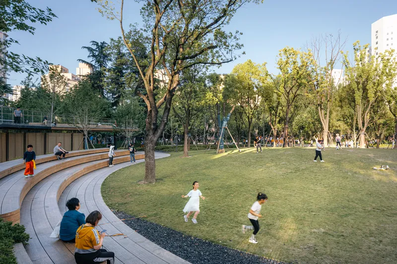 Curved timber amphitheater steps descending toward a lawn where children play among mature trees