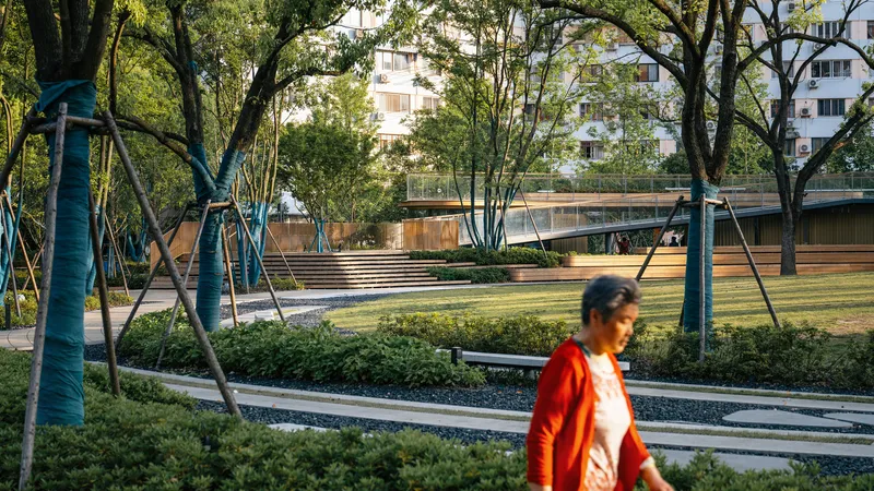 Pathway through the park with preserved tree trunks, low shrubs, and a woman in orange passing through
