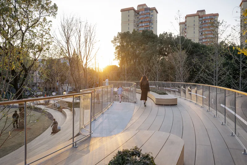 Curving timber boardwalk with glass railings and stone benches at sunset